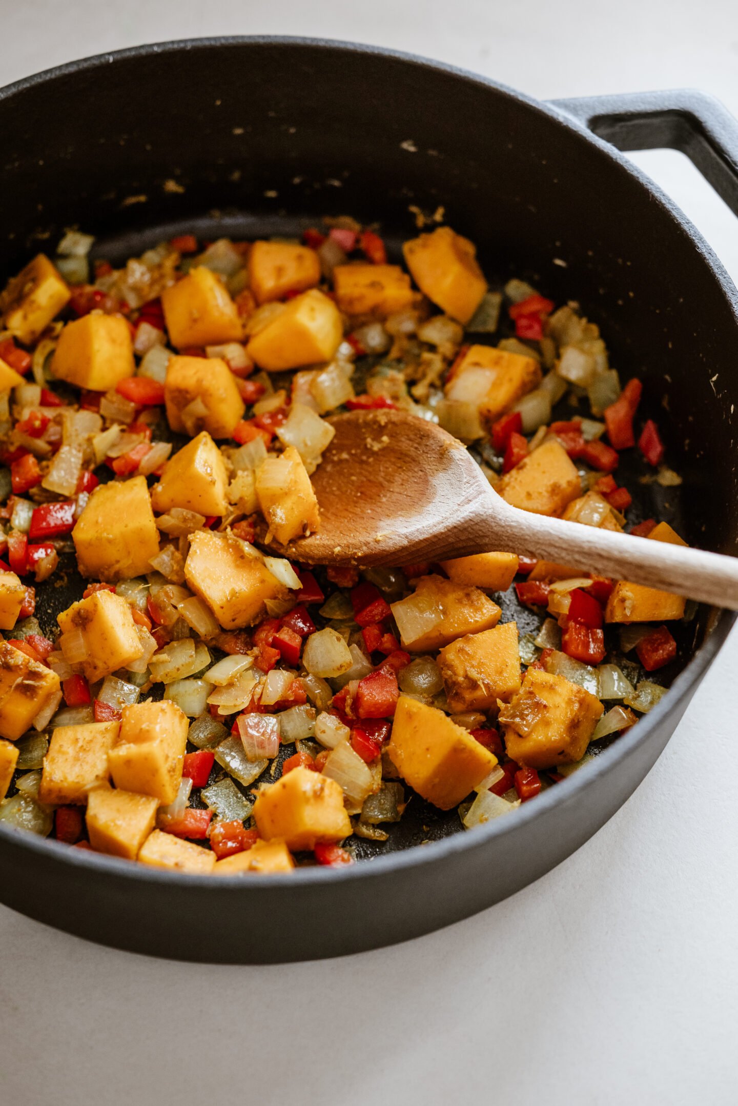 A pot sautes onions, peppers and squash as a wooden spoon stirs.
